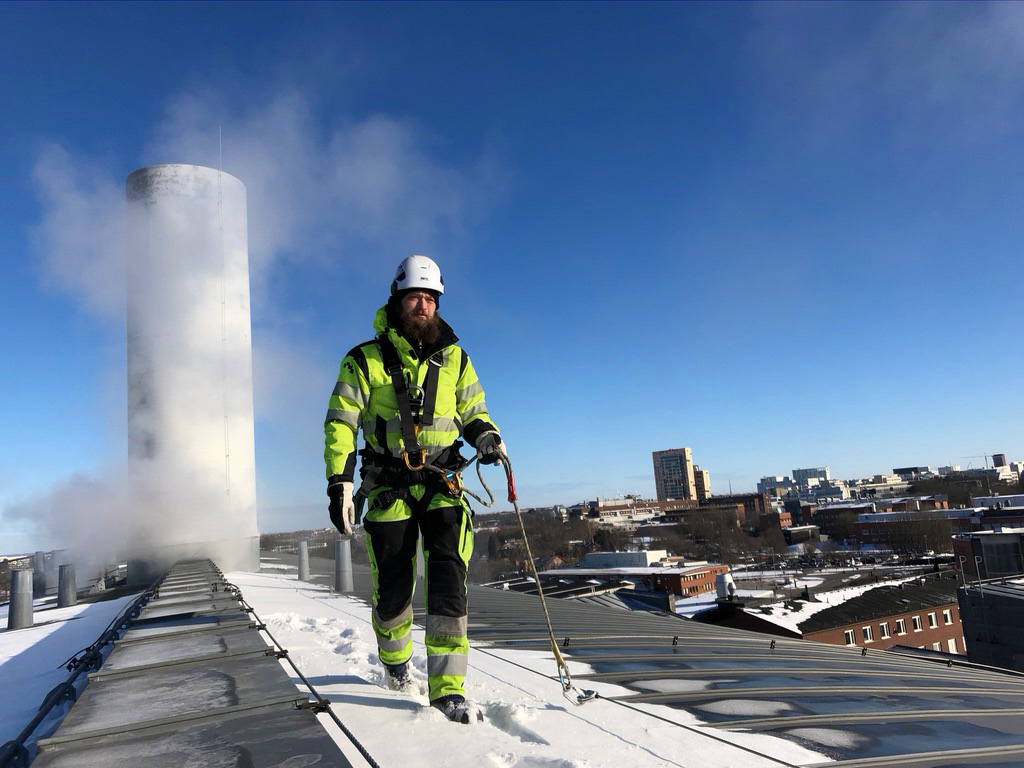 arbetare går på tak med sele, på taket ligger även snö