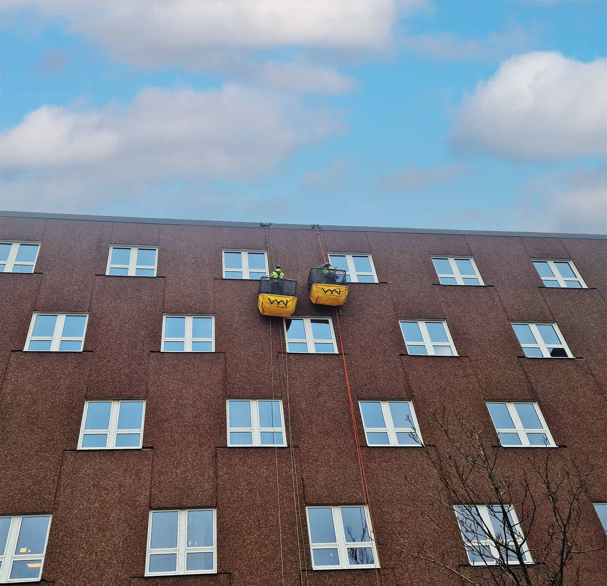 två arbetsburar hängandes i lina vid fasadarbete