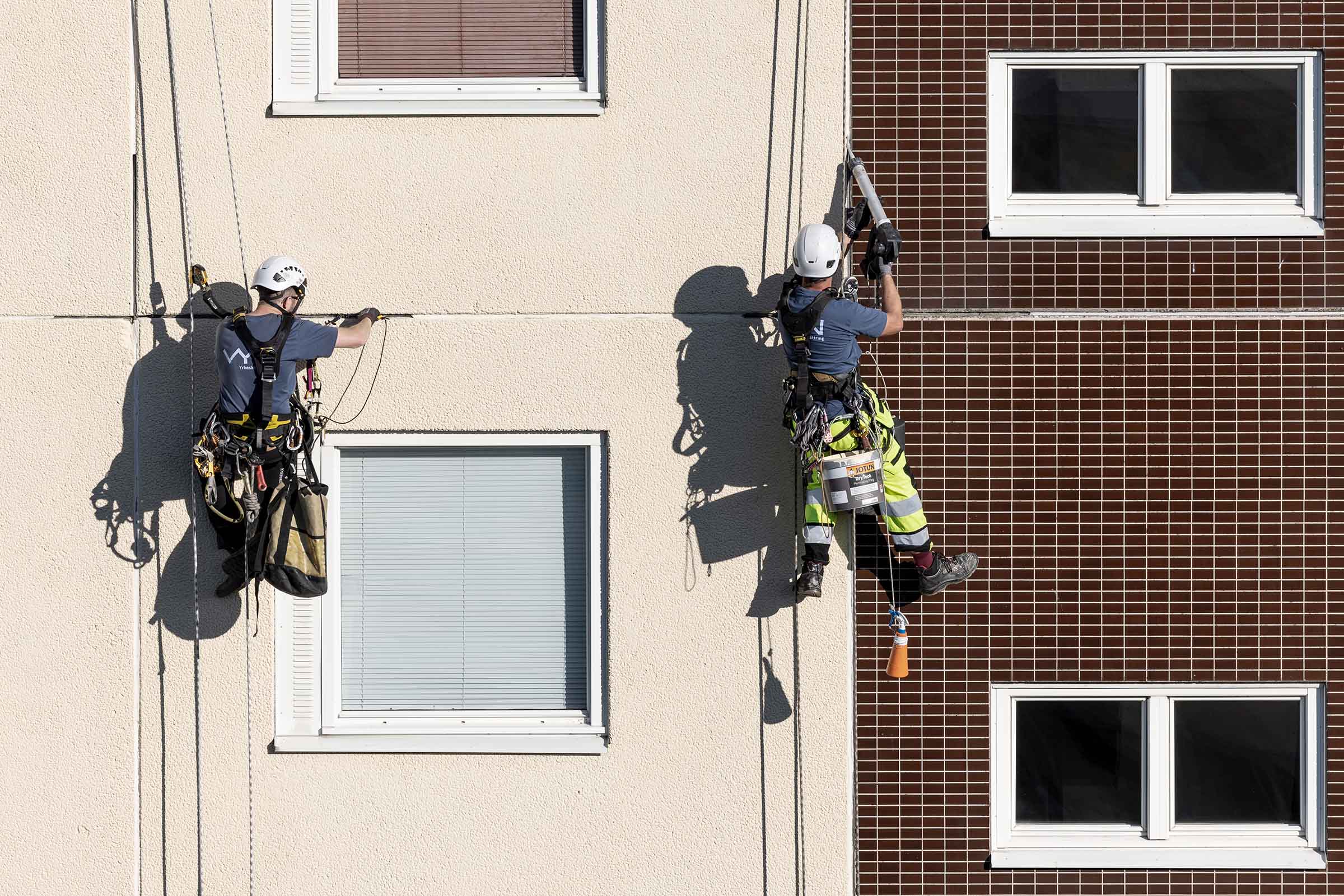 två personer hängandes i sele fogar i fasaden