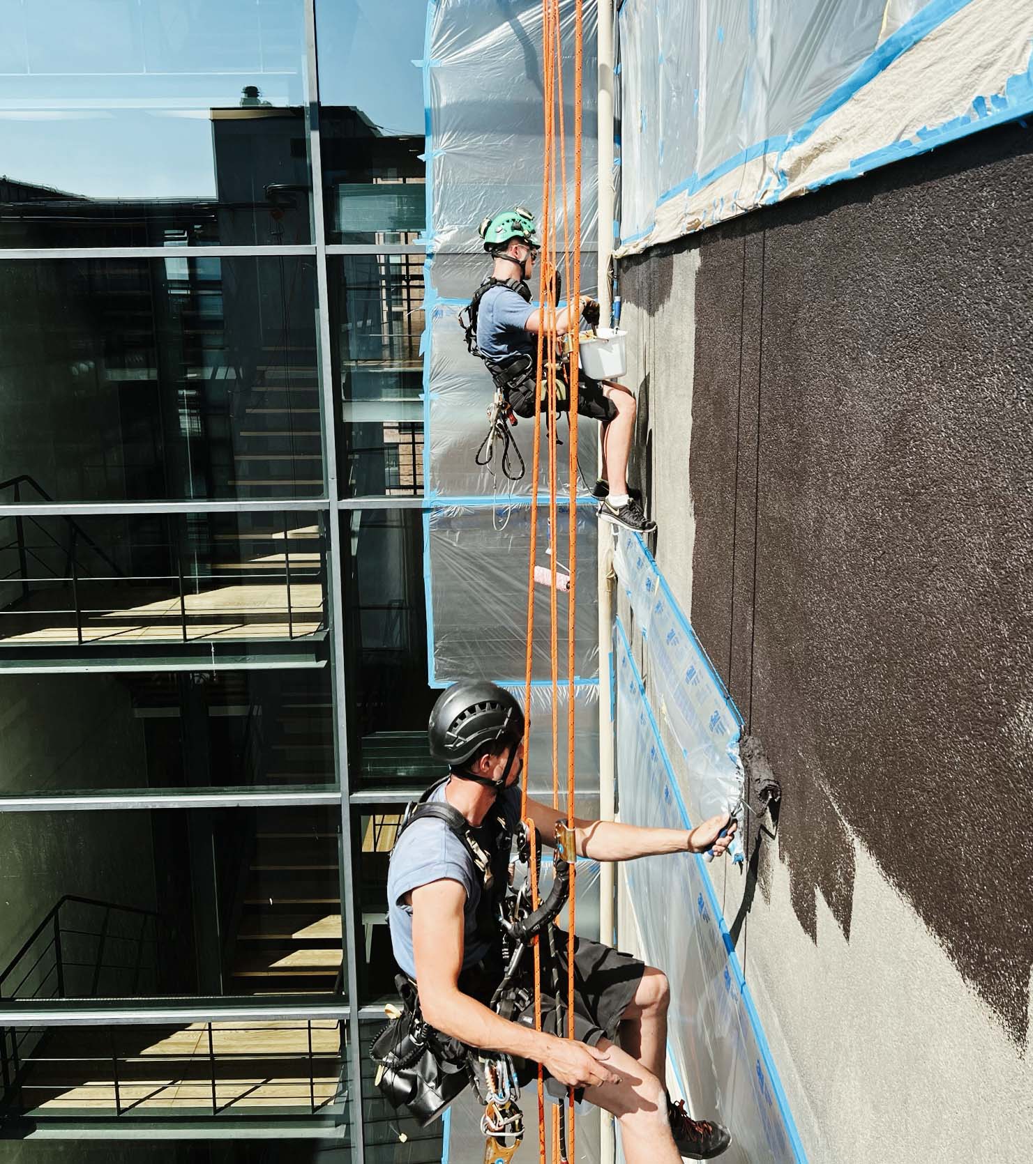 arbetare hängandes i sele och utför målningsarbete