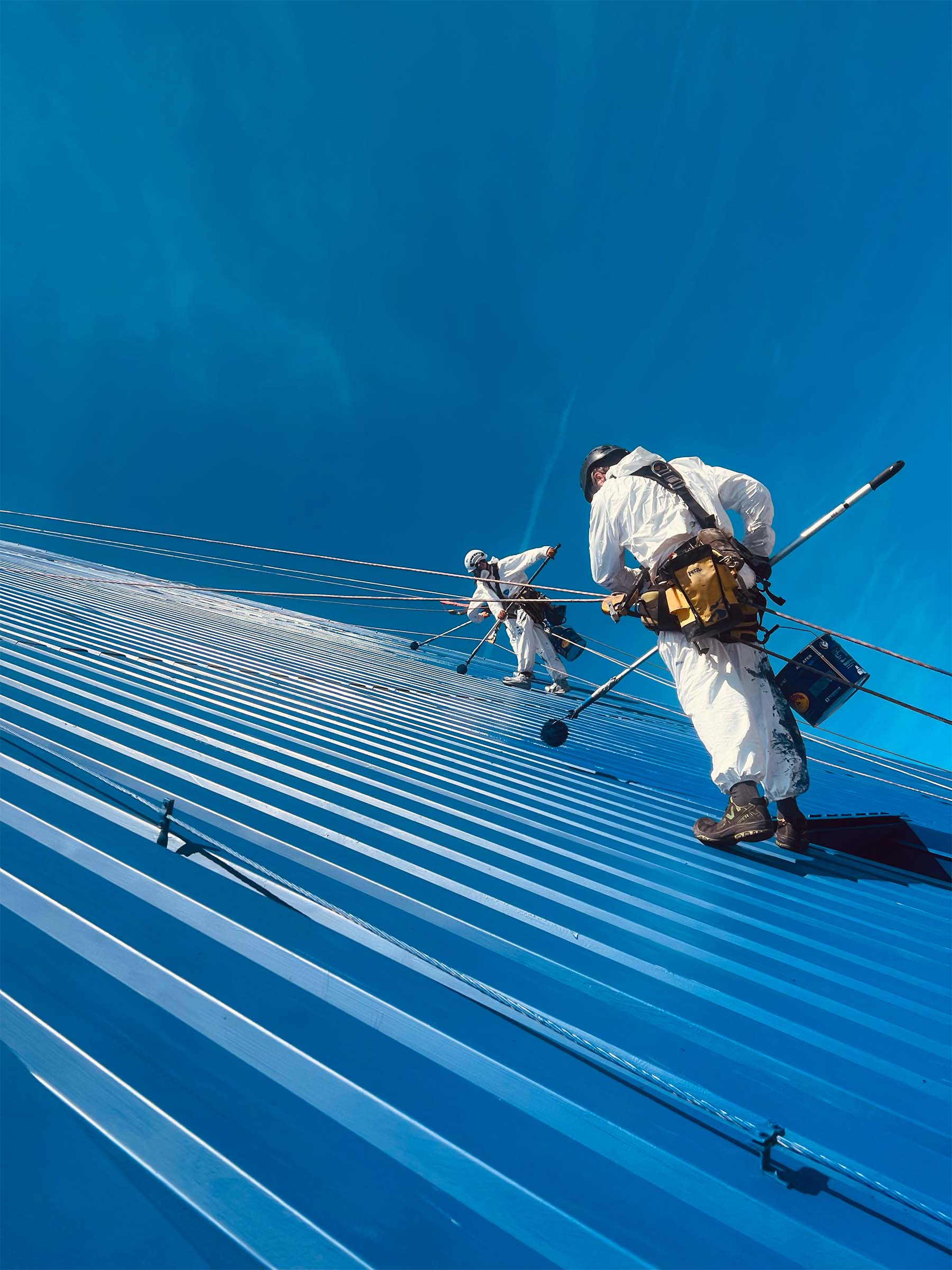 två personer hängandes i sele på fasad med solnedgång i bakgrunden