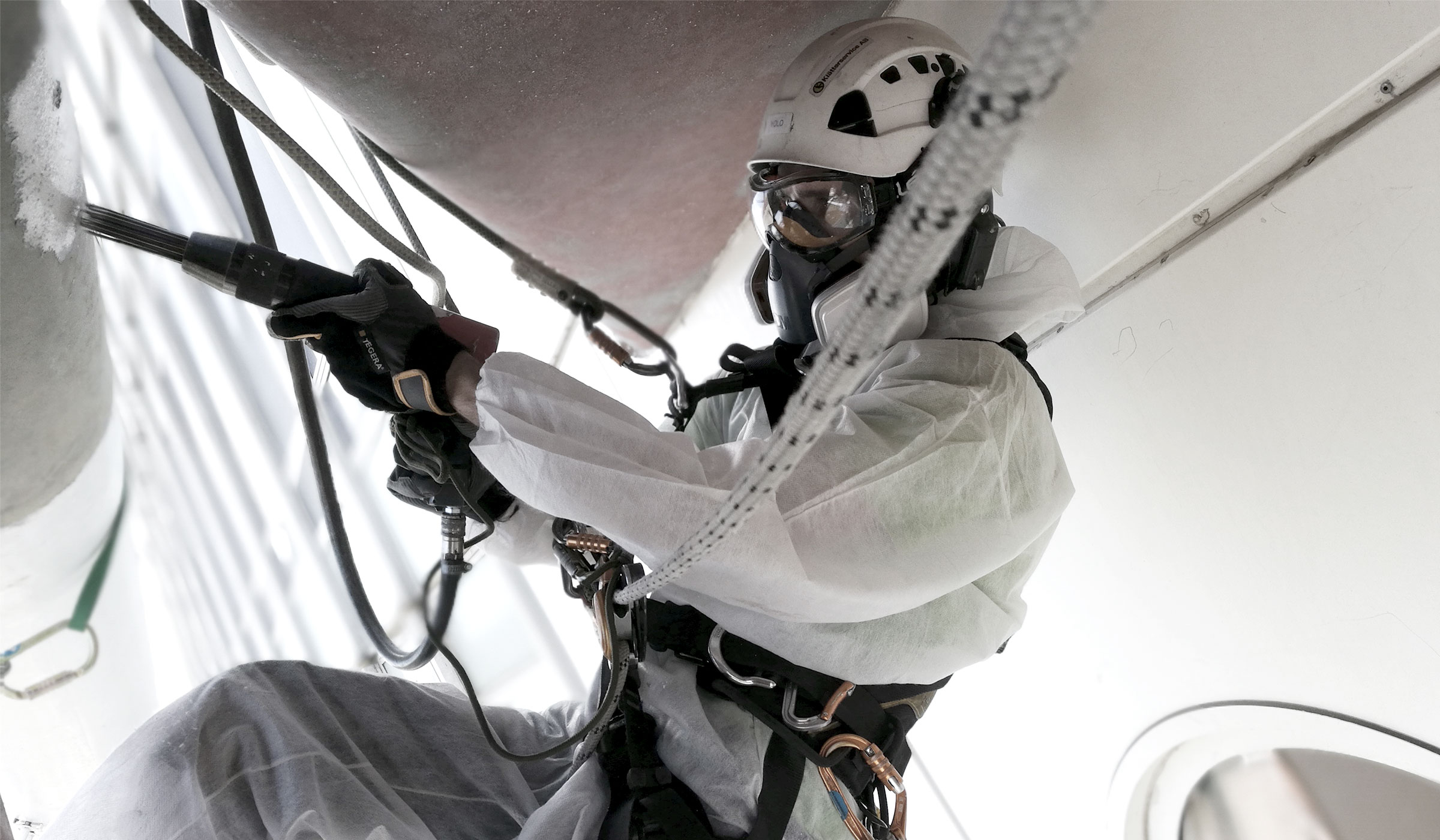 närbild på maskerad arbete som utför rostskyddsmålning hängandes i sele